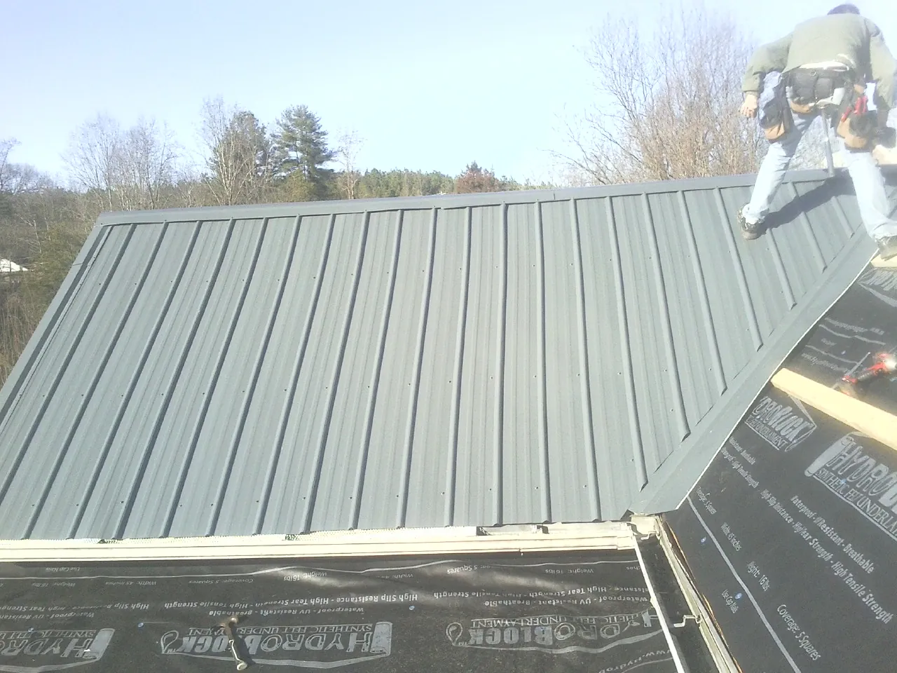 Crew installing dark green standing seam panels over synthetic underlayment in Pikeville