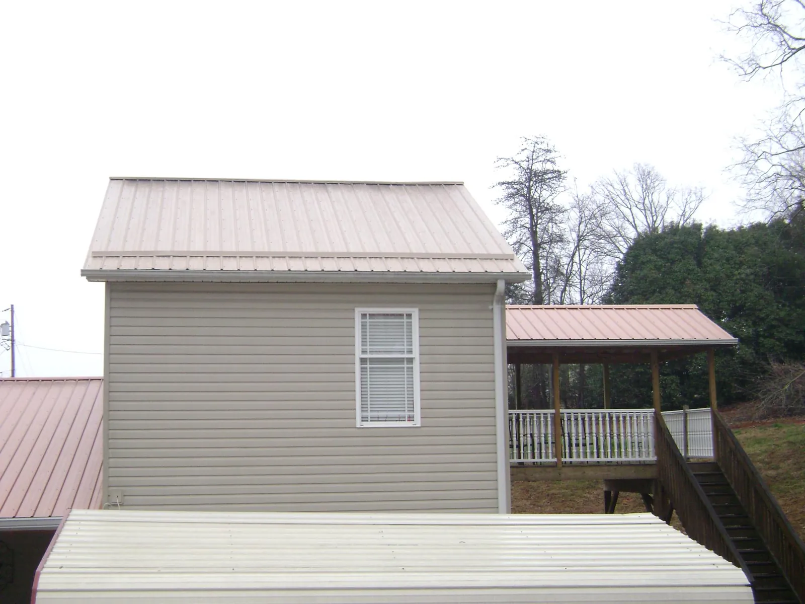 Tan metal roofs on a two story addition and attached porch, from a Roof Replacement job in Pikeville